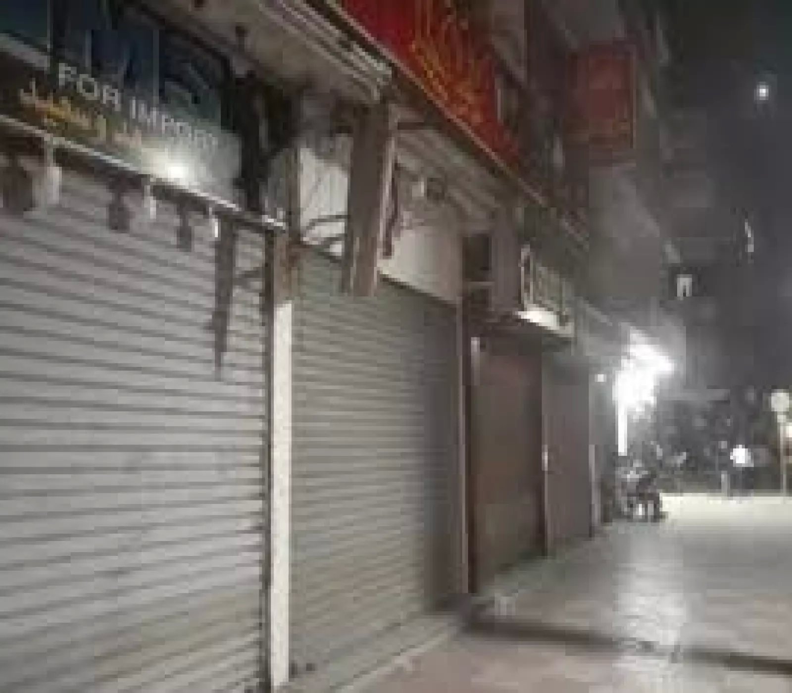 صف لمحلات تجارية مغلقة بأبواب معدنية منزلقة في شارع ليلي هادئ بإضاءة خافتة.